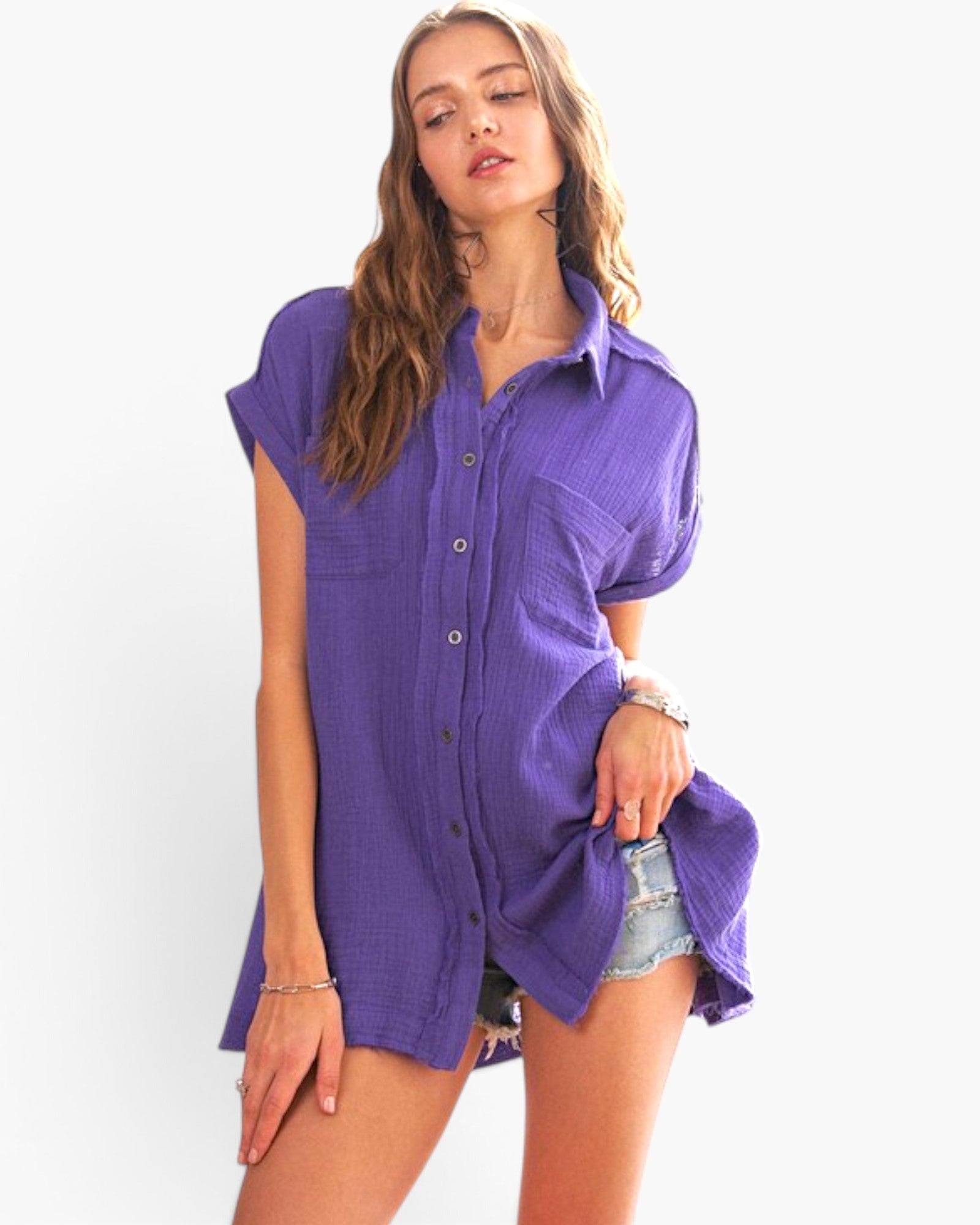 A woman modeling a purple short-sleeve button-up shirt with a textured crinkle fabric, paired with denim shorts, against a plain white background.