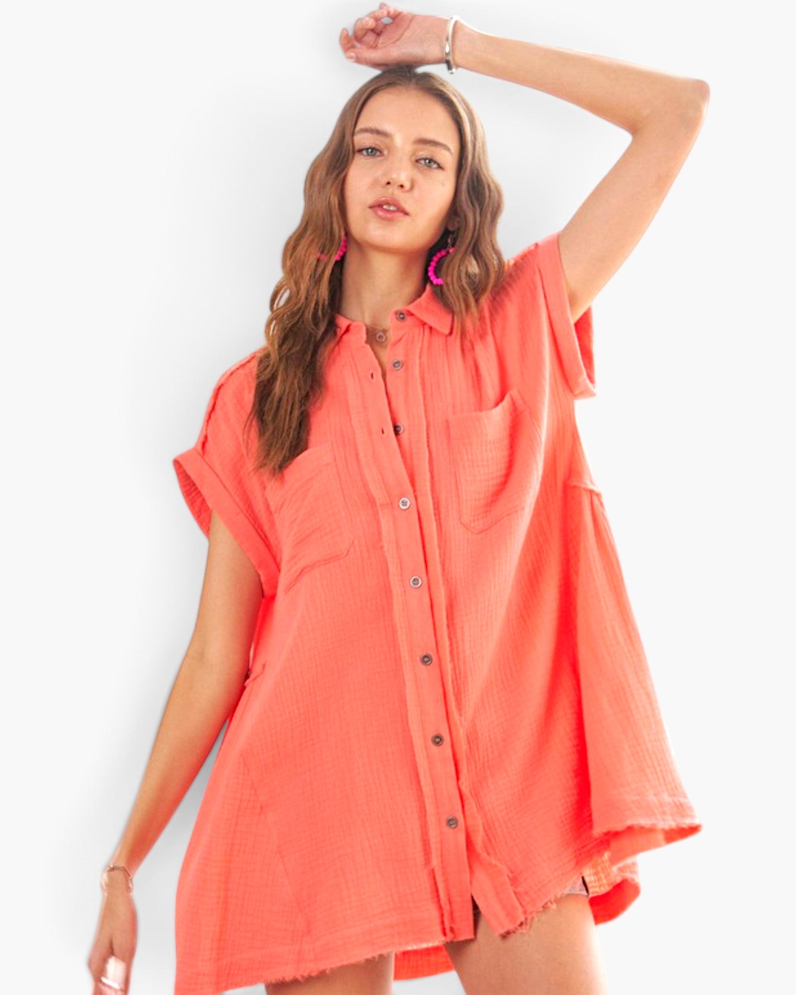A woman modeling a short-sleeve, button-front shirt dress in a bright coral-orange color against a clean white background.