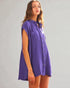 Woman wearing a purple sleeveless shirt dress against a gray background