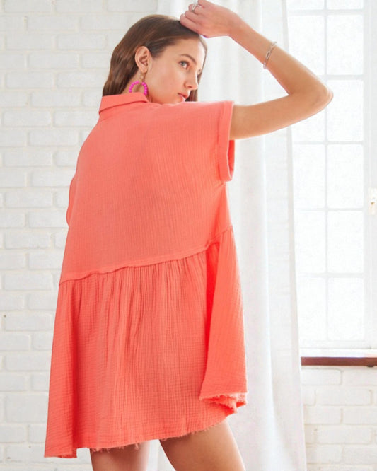 Woman wearing a coral dress against a white brick wall.