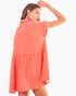 A woman modeling a short-sleeve coral pink textured dress with a tiered ruffle design, shown from a three-quarter back angle against a plain white background.