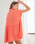 Woman wearing a coral dress against a white brick wall.
