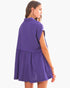 A woman wearing a purple sleeveless mini dress with a tiered skirt, shown from a three-quarter back view against a plain white background.