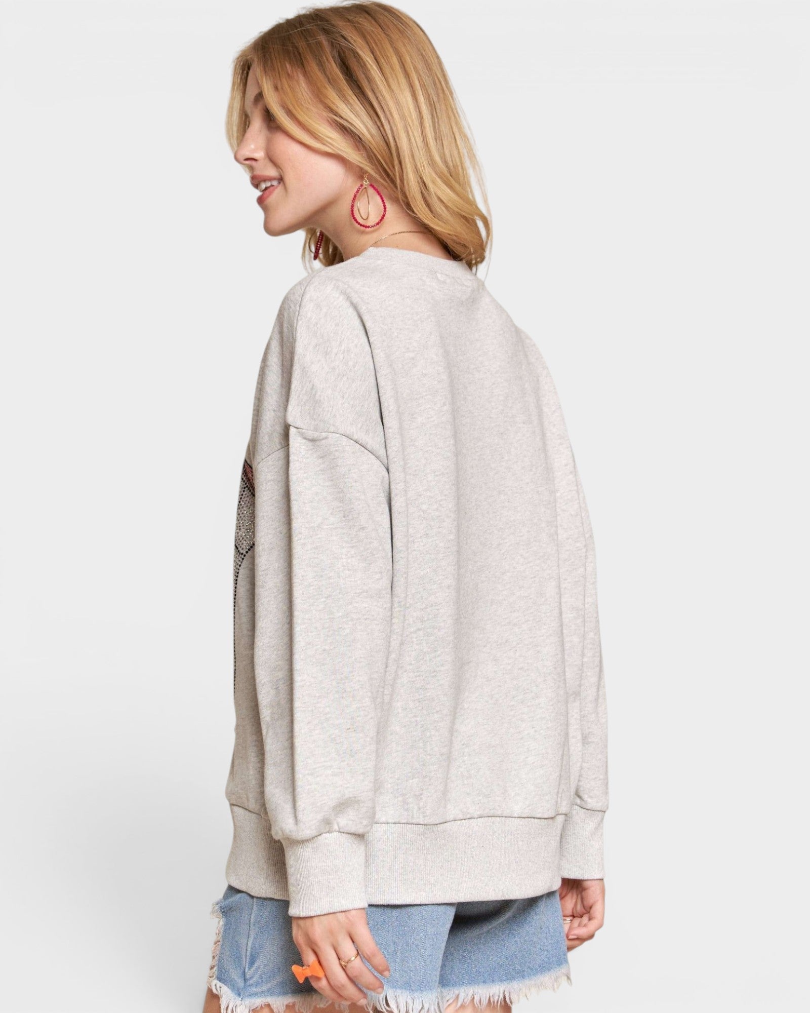 Woman wearing a light gray sweatshirt and denim shorts on a white background