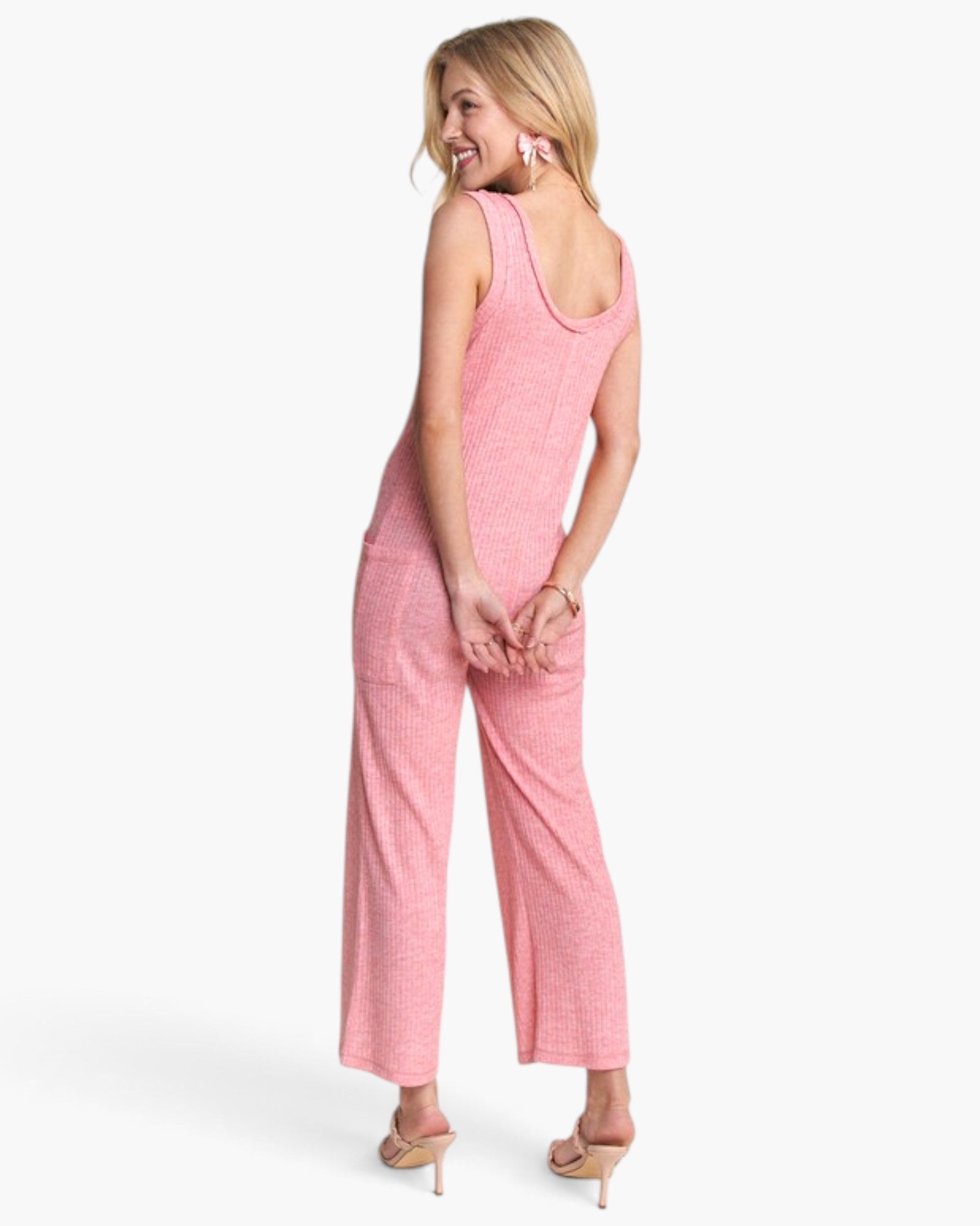 A woman modeling a pink sleeveless jumpsuit with wide legs, shown from a three-quarters back angle against a clean white background.