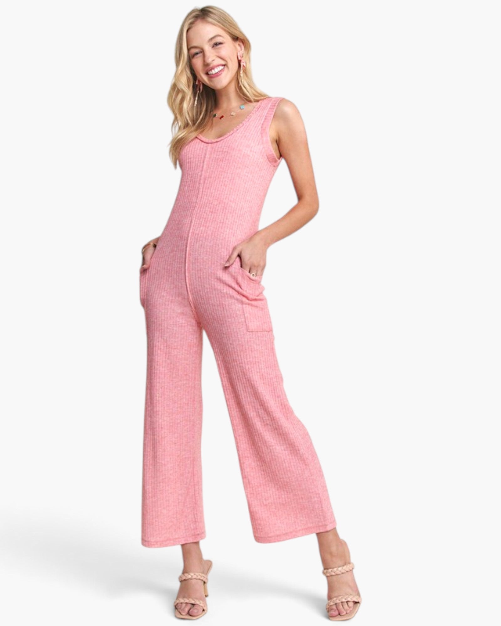 A woman modeling a pink sleeveless wide-leg jumpsuit with front pockets, photographed against a clean white studio background.