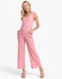 A woman modeling a pink sleeveless wide-leg jumpsuit with front pockets, photographed against a clean white studio background.