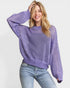 Woman wearing a purple open-knit sweater and light blue jeans on a white background