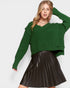 Woman wearing a green sweater and black pleated skirt on a white background