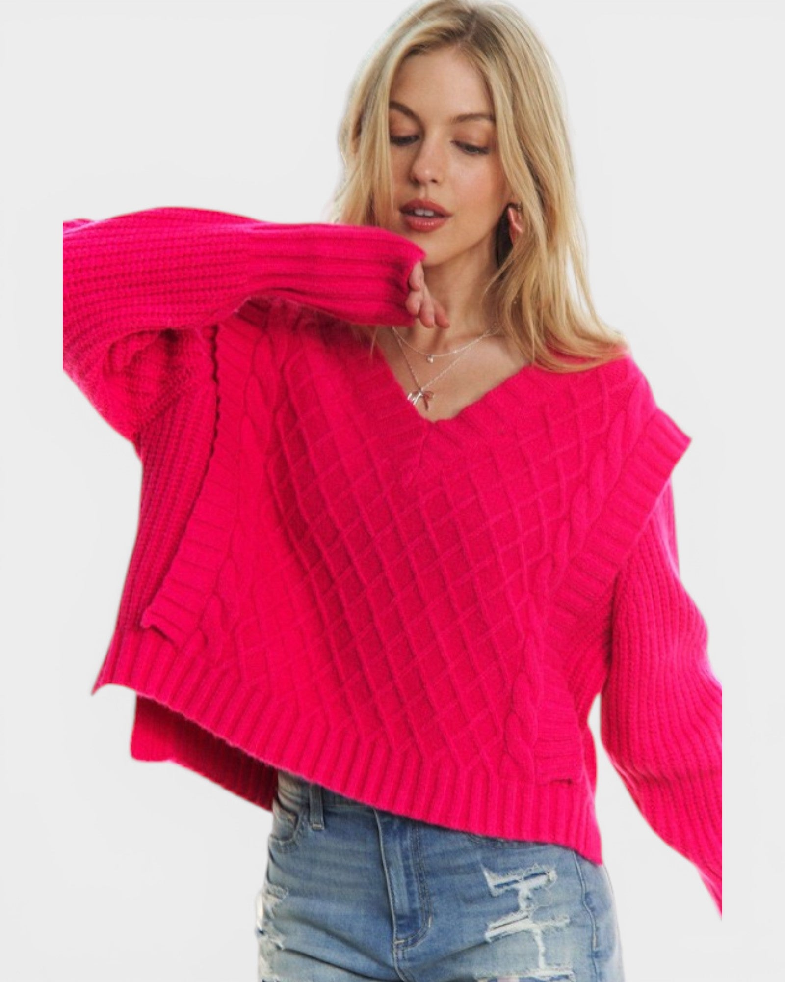 Woman wearing a bright pink sweater and blue jeans on a white background