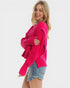 Woman wearing a bright pink cardigan over a denim shirt on a white background