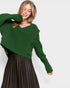 Woman wearing a green sweater and black pleated skirt on a white background
