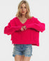 Woman wearing a bright pink sweater and denim shorts on a white background