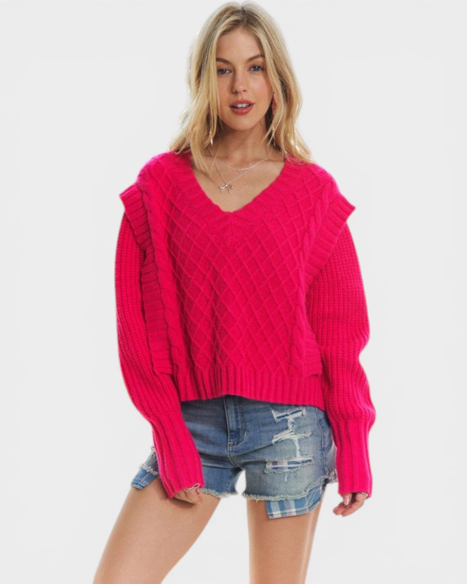 Woman wearing a bright pink sweater and denim shorts on a white background