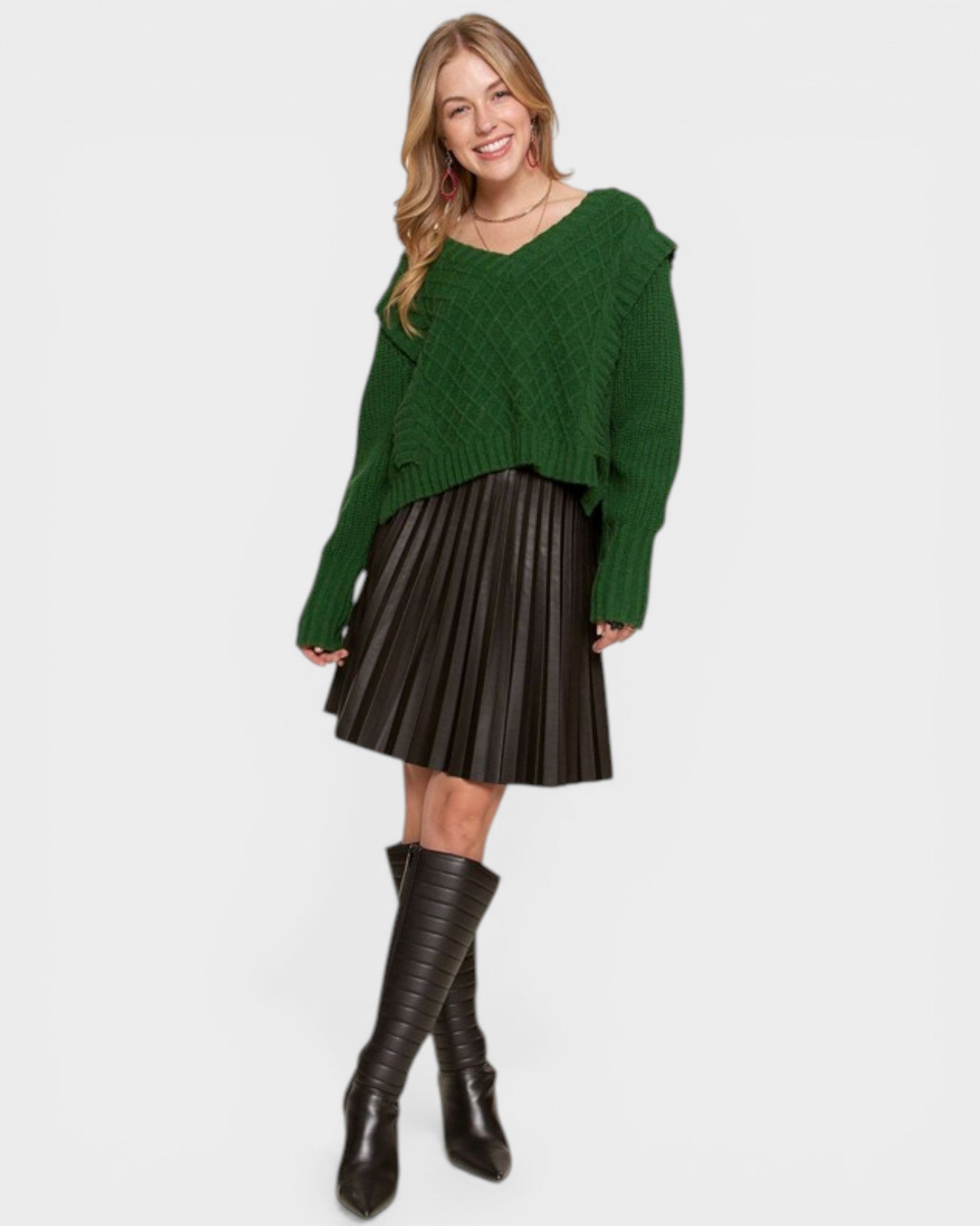 Woman wearing a green sweater and black pleated skirt with brown boots on a white background