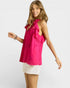 Woman wearing a bright pink sleeveless top with ruffle details on a white background