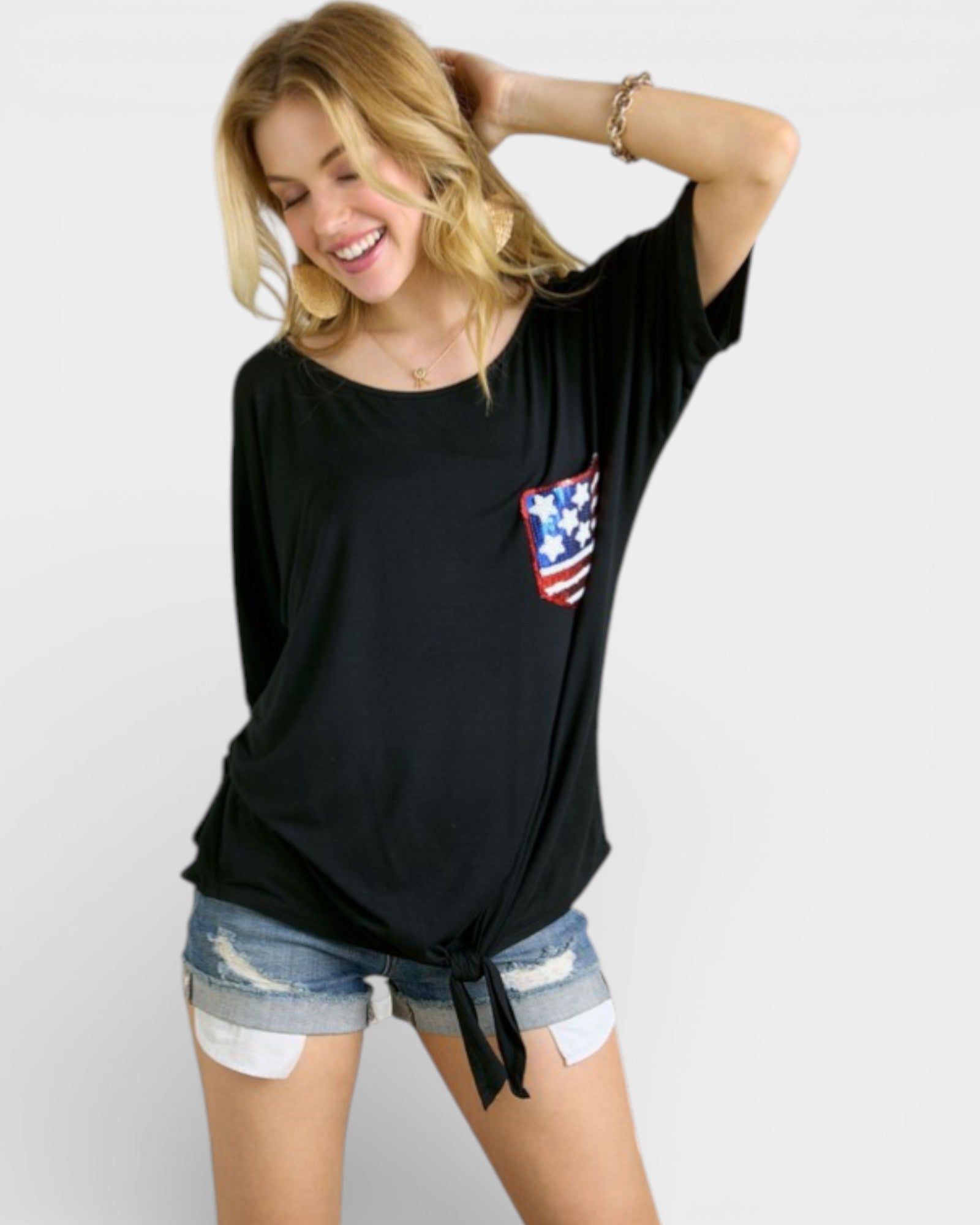 Woman wearing a black t-shirt with an American flag design and denim shorts on a white background