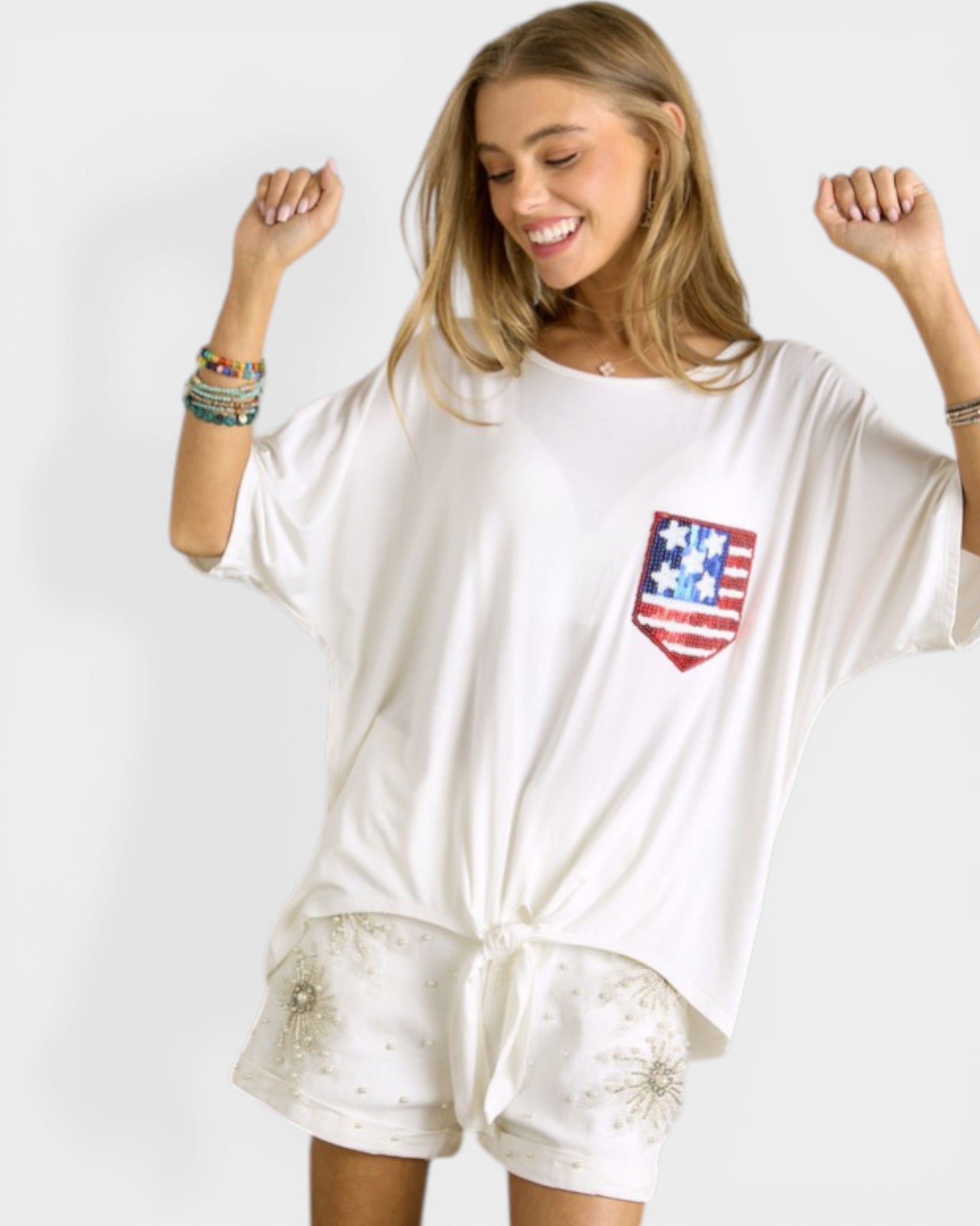 Woman wearing a white oversized shirt with an American flag pocket design on a plain background