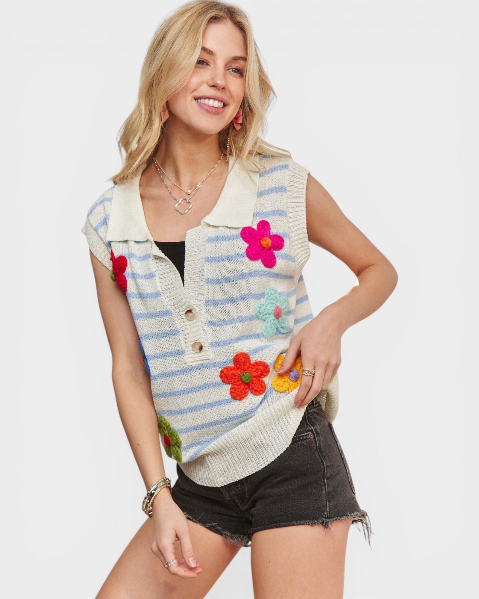 Woman wearing a colorful striped vest with floral designs on a plain background