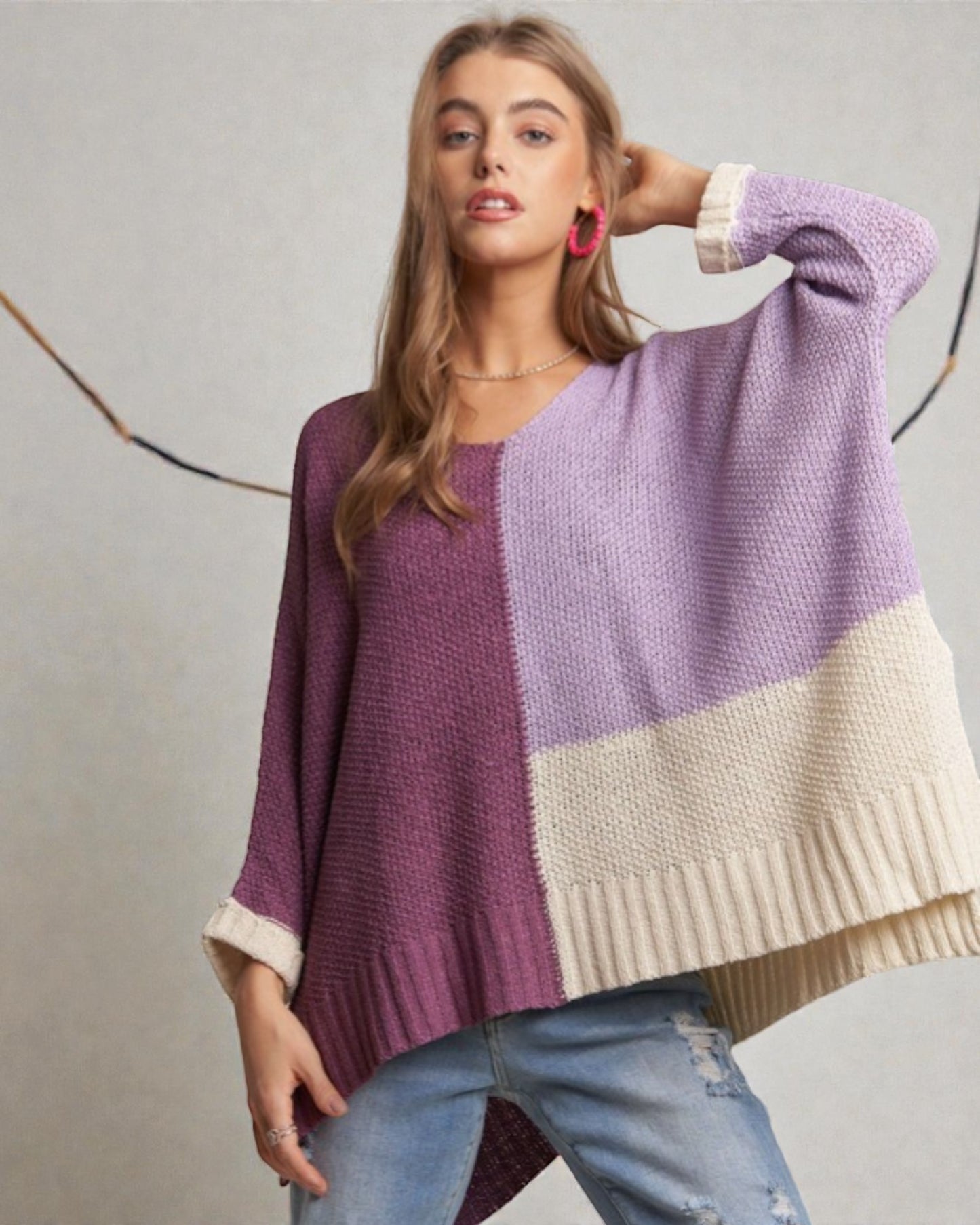 Woman wearing a color-blocked sweater with purple, white, and beige sections on a neutral background.