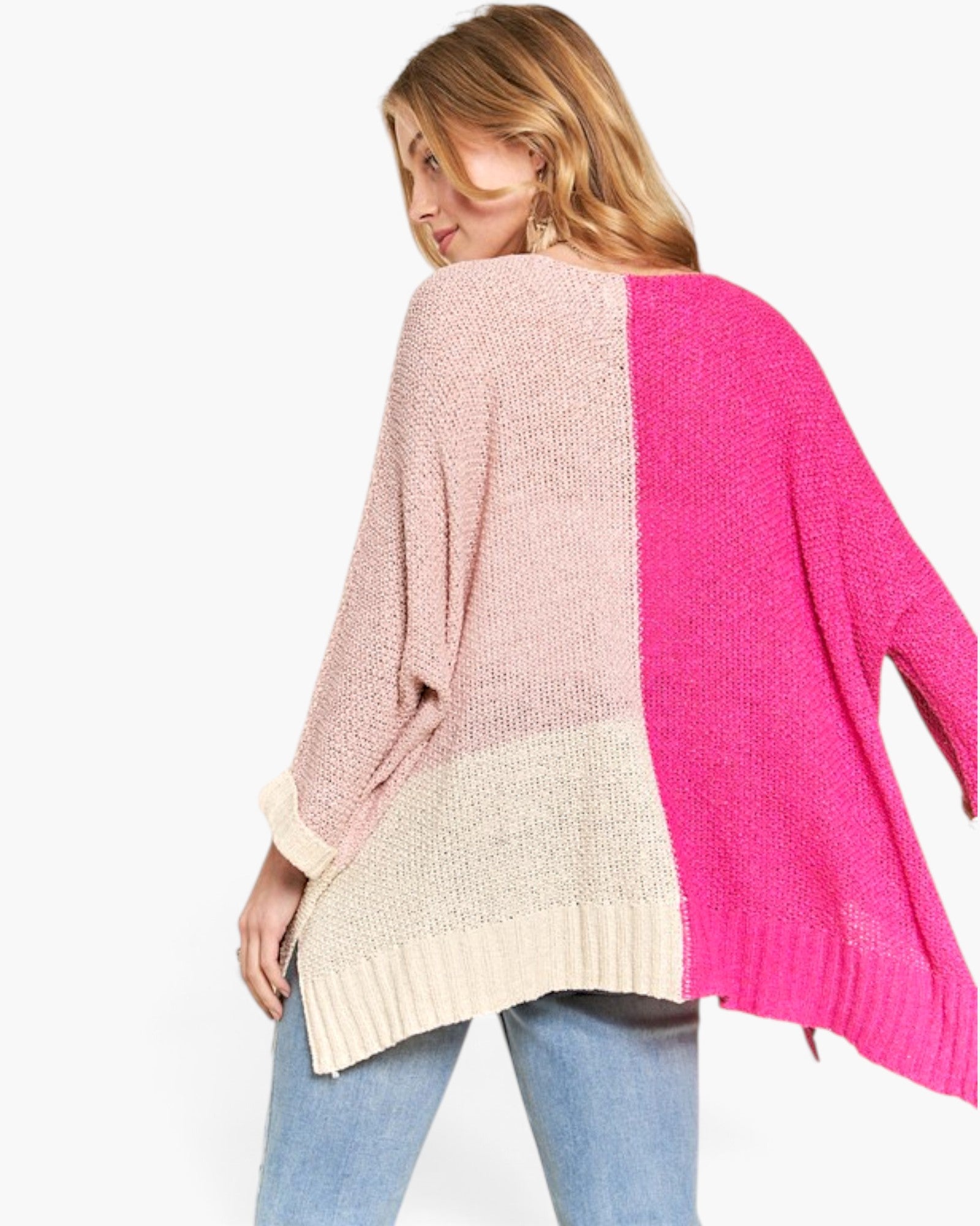 A woman wearing a chunky knit colorblock sweater with pink, cream, and bright magenta panels, paired with blue jeans, shown from a back-three-quarter view against a plain white background.