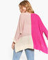A woman wearing a chunky knit colorblock sweater with pink, cream, and bright magenta panels, paired with blue jeans, shown from a back-three-quarter view against a plain white background.