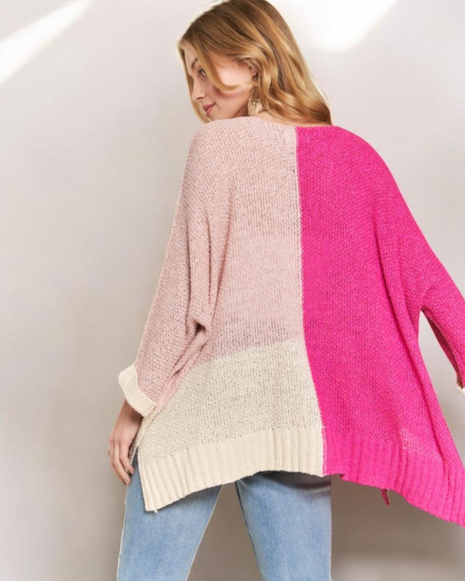Woman wearing a color-blocked sweater with pink, beige, and white sections on a plain background.