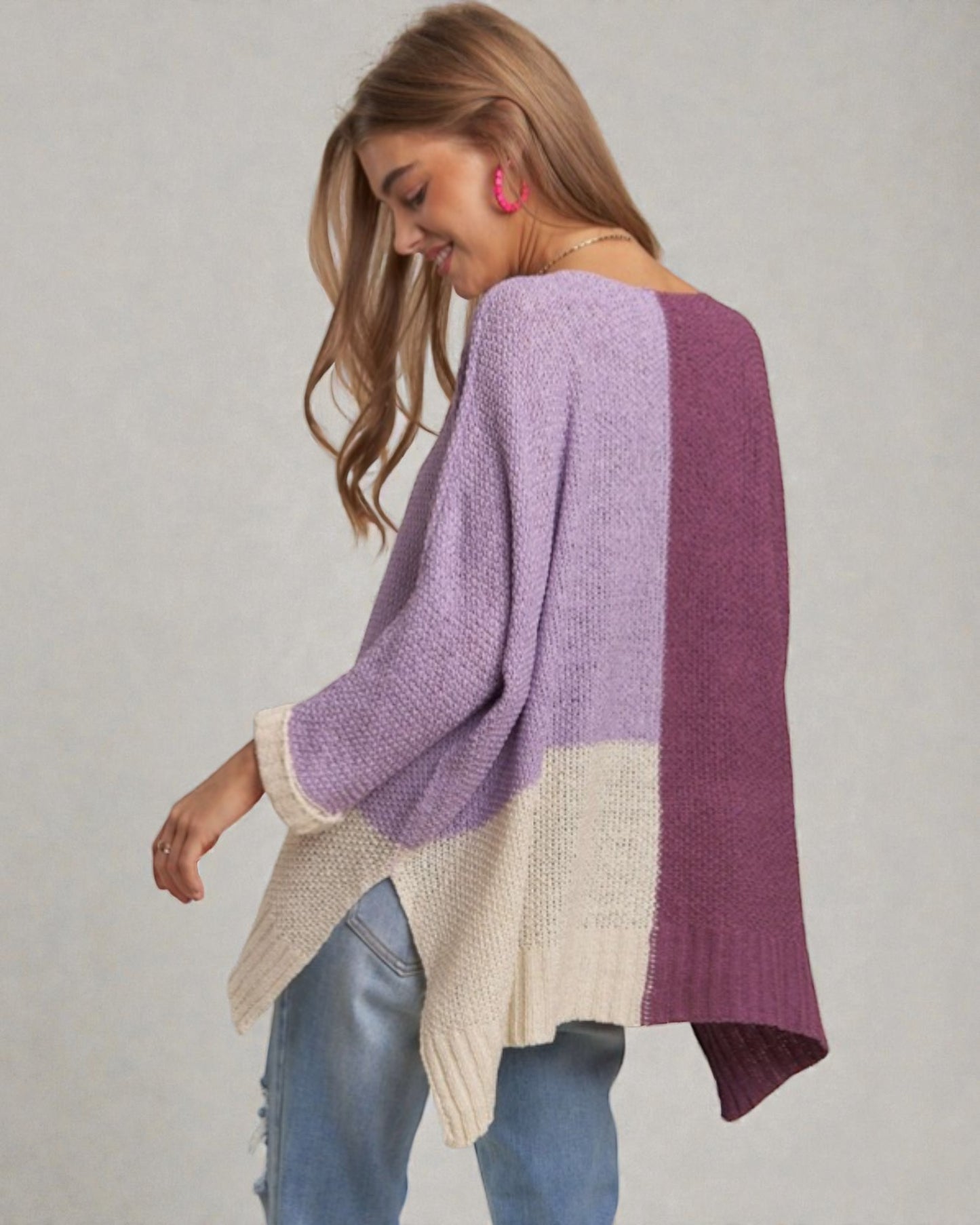 Woman wearing a color-blocked sweater with purple, beige, and blue sections on a plain background.