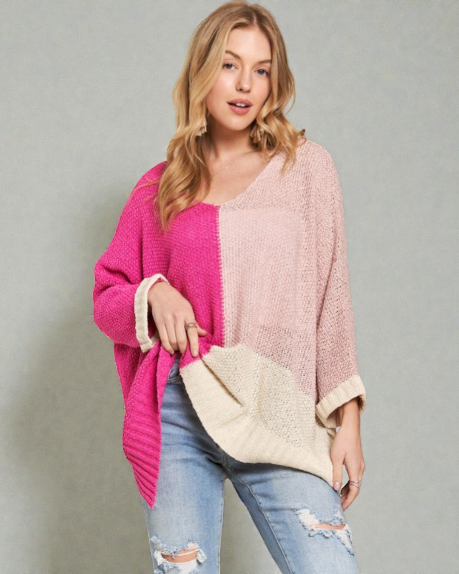 Woman wearing a pink and white sweater with a beige clutch against a gray background