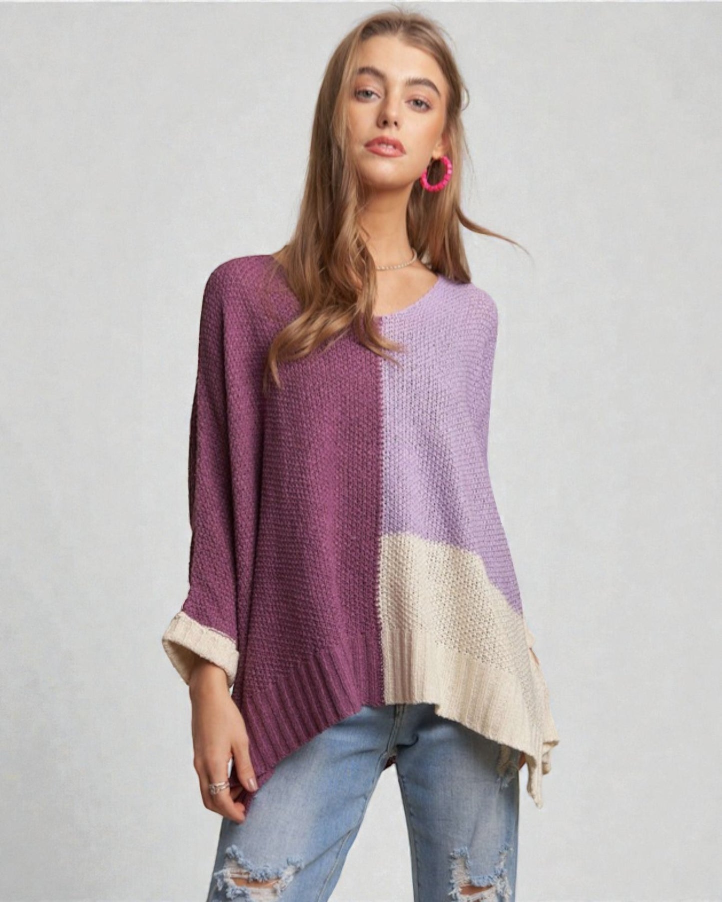 Woman wearing a two-tone purple and beige sweater with ripped jeans on a plain background
