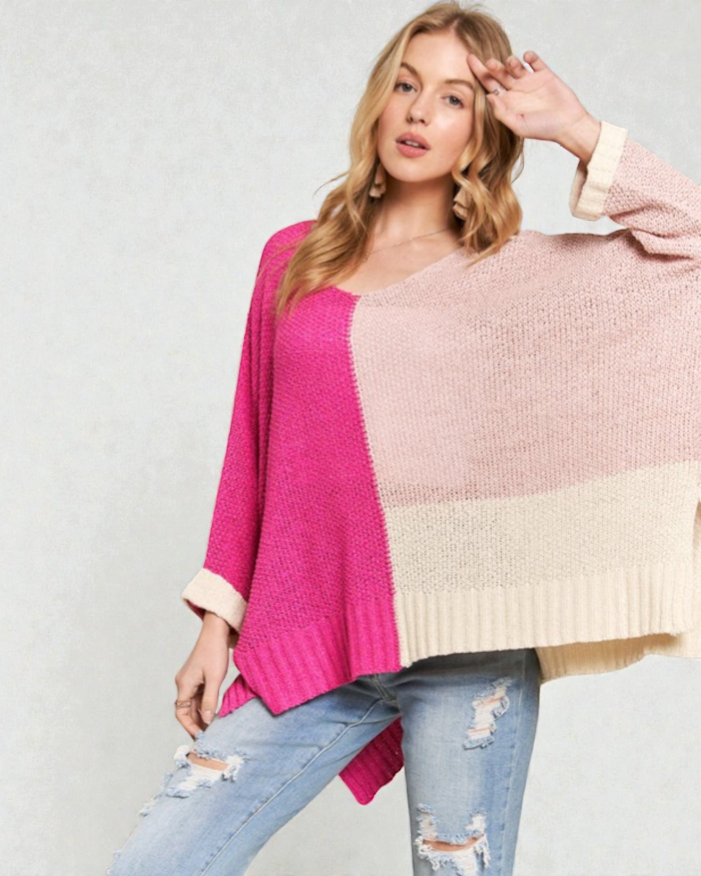 Woman wearing a color-blocked sweater with pink, beige, and blue sections on a light gray background.