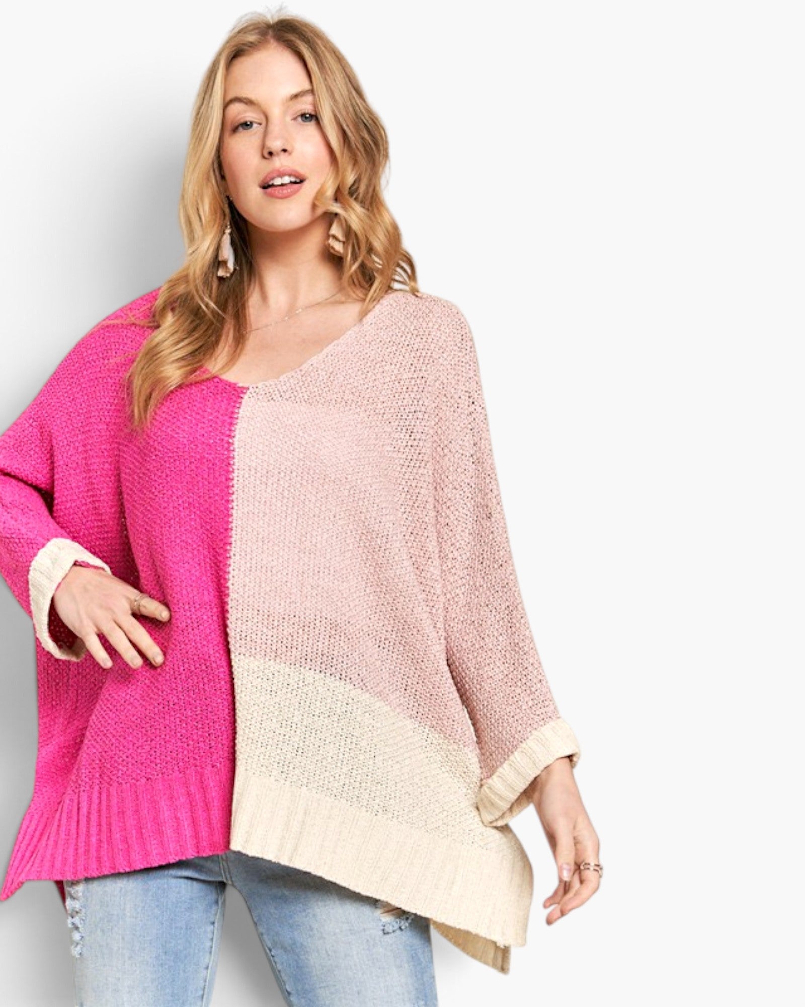 A woman wearing a chunky knit colorblock sweater with bright pink, dusty pink, and cream panels, paired with blue jeans, against a plain white background.