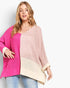 A woman wearing a chunky knit colorblock sweater with bright pink, dusty pink, and cream panels, paired with blue jeans, against a plain white background.