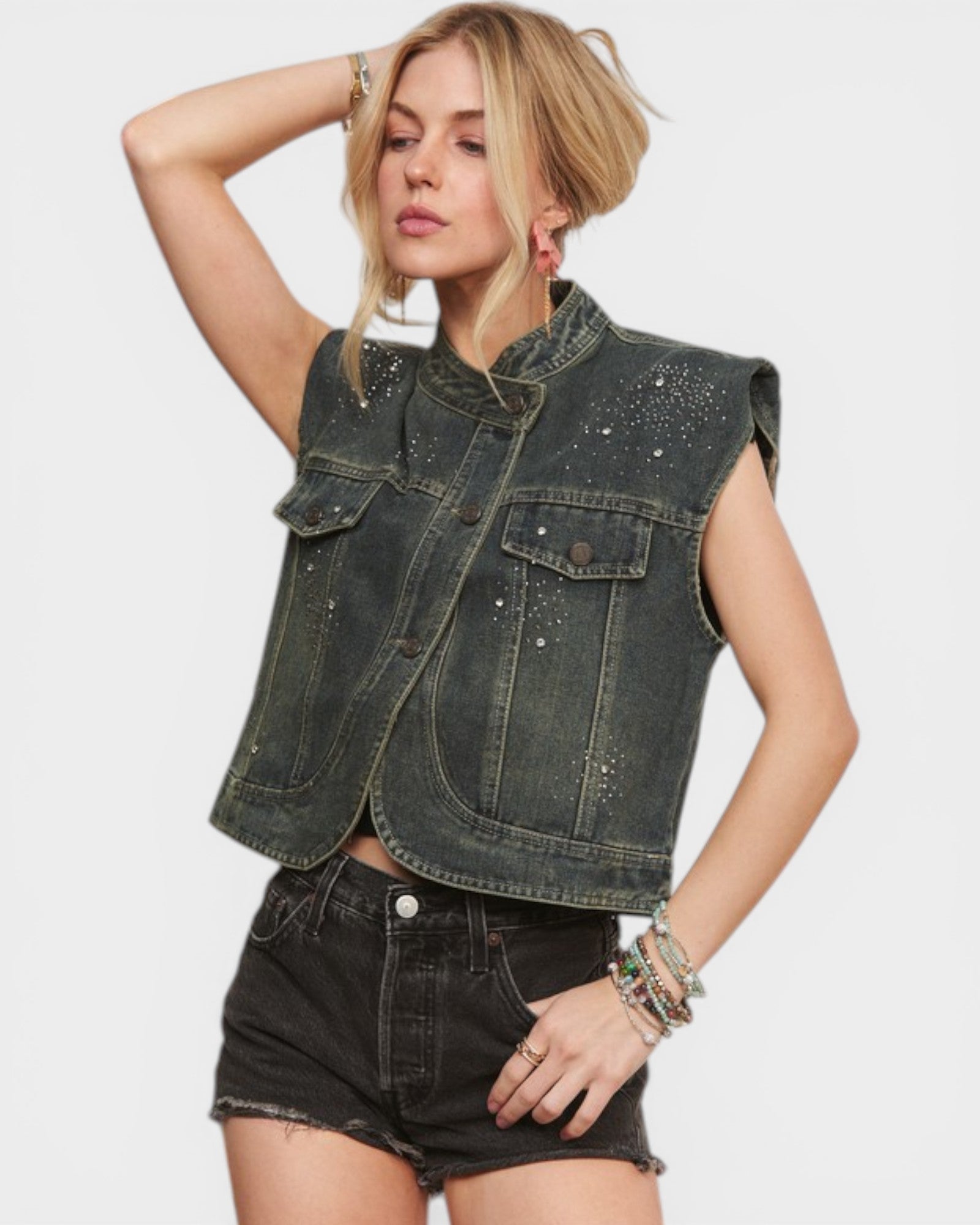 Woman wearing a denim vest with embellishments on a plain background