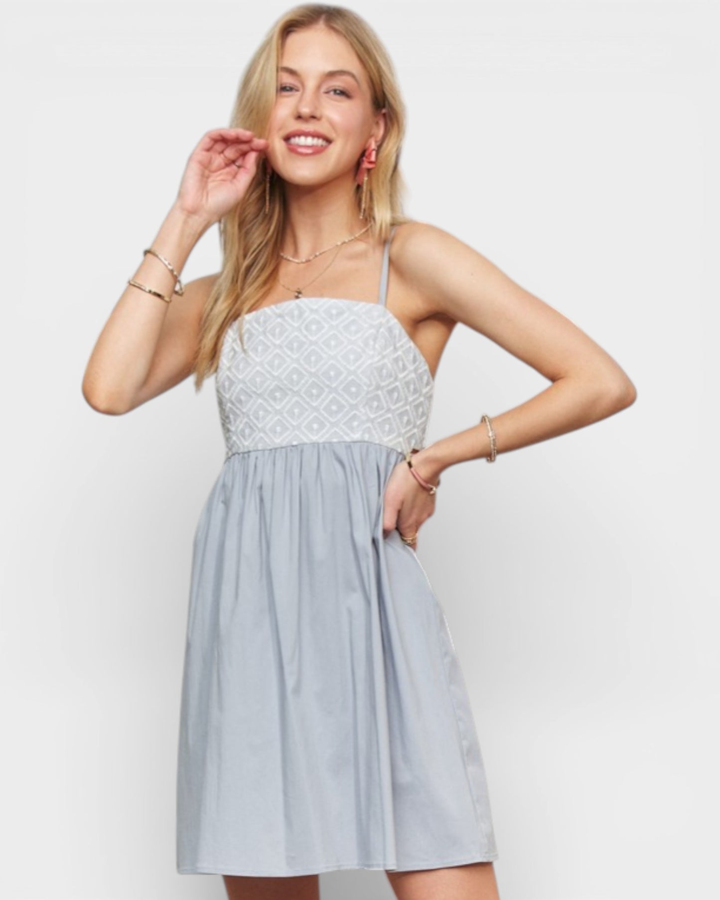 Woman wearing a light blue dress with a white lace top against a plain background