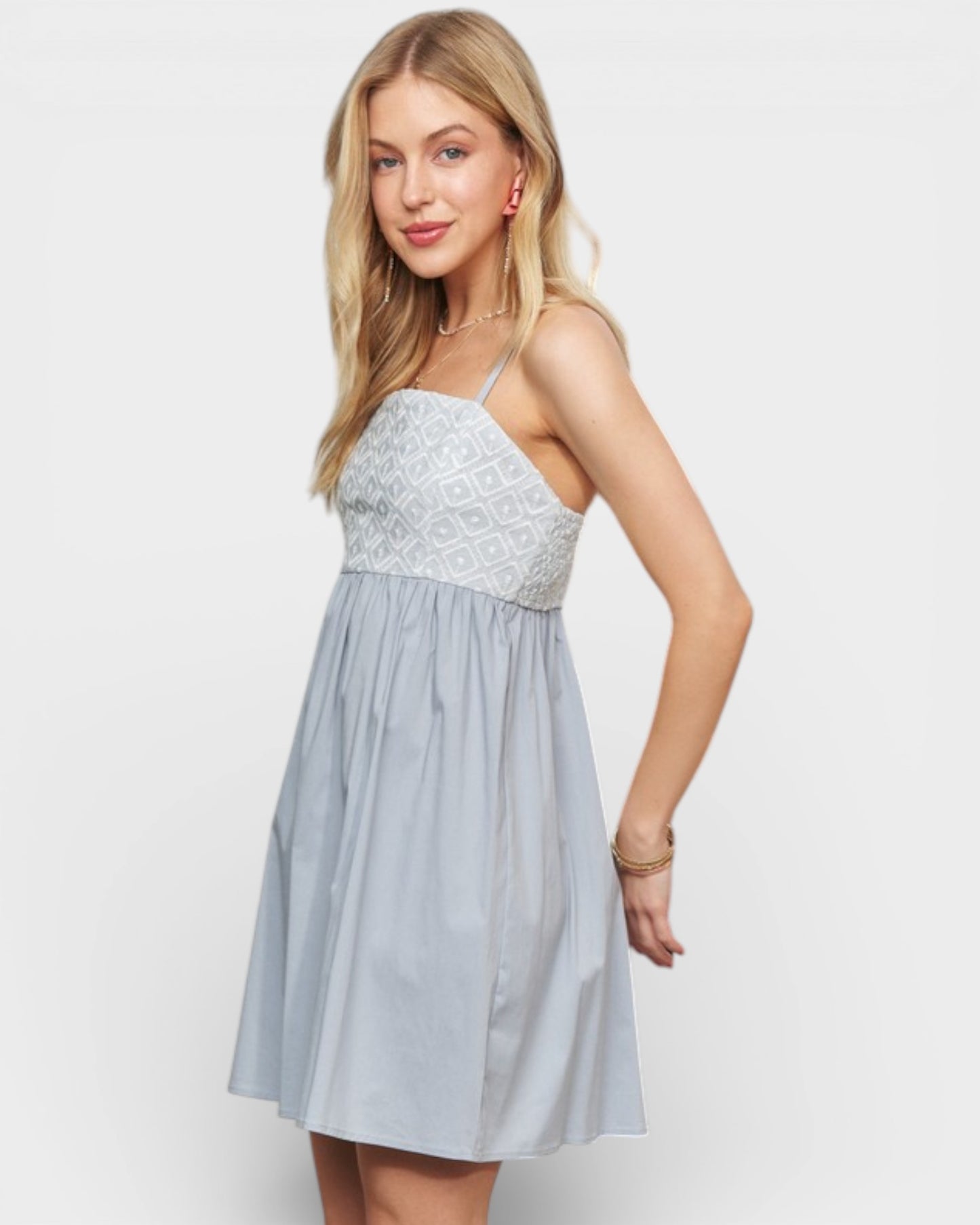 Woman wearing a light blue dress with a white lace top on a plain background