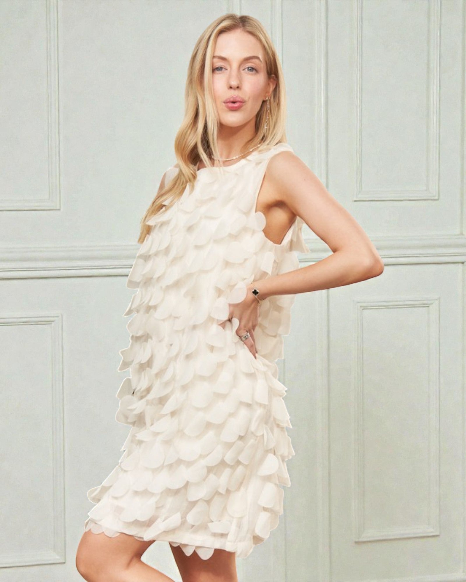 Woman wearing a white dress with floral details against a light blue wall.