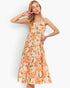 A woman modeling a sleeveless, tiered midi dress with a peach and orange floral print with green leaves, set against a plain white studio background.