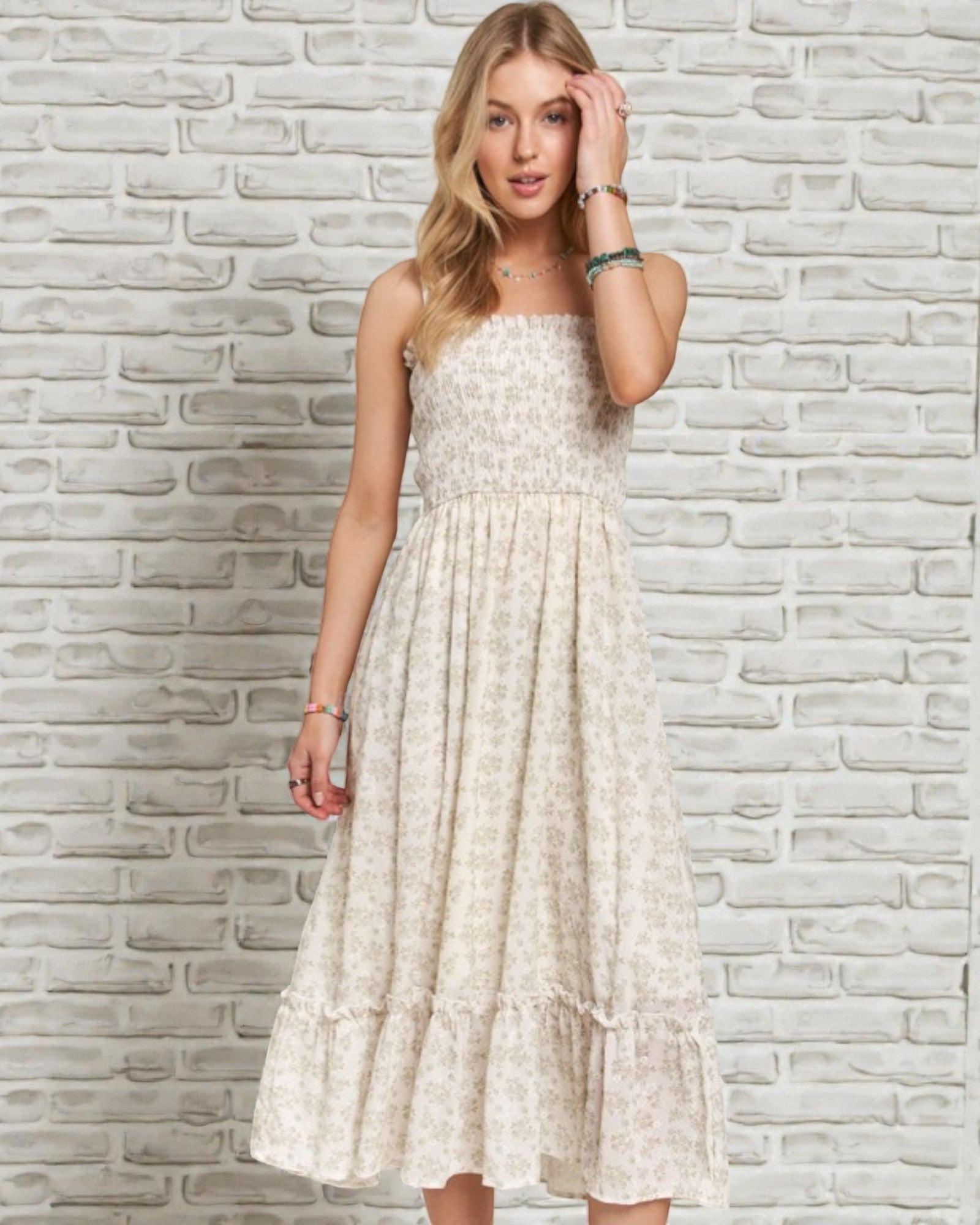 Woman wearing a white floral dress against a textured stone wall.