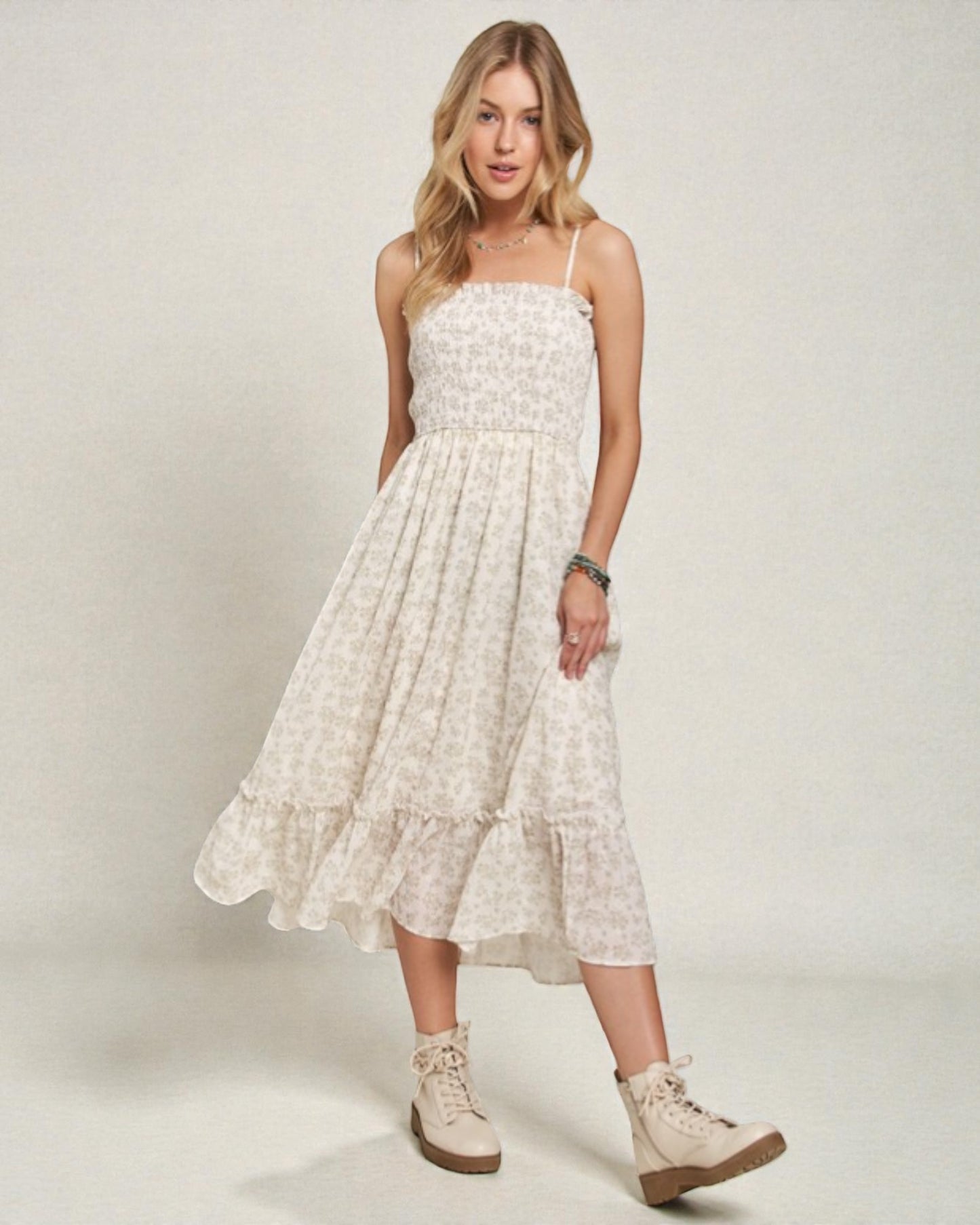 Woman wearing a white floral dress with beige boots on a plain background