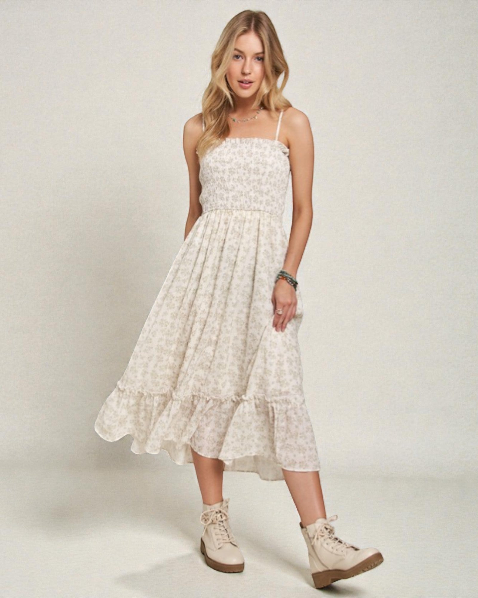 Woman wearing a white floral dress with beige boots on a plain background