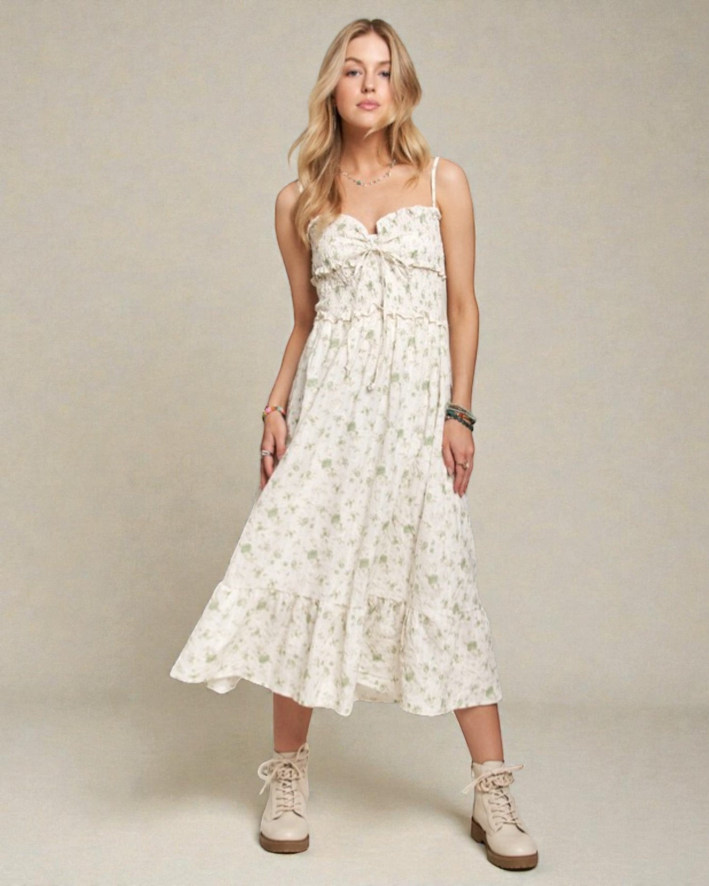 Woman wearing a white floral dress with beige boots on a plain background