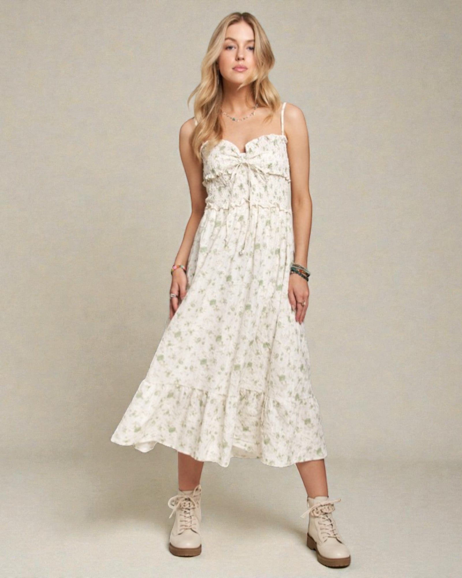 Woman wearing a white floral dress with beige boots on a plain background