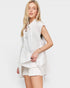 Woman wearing a white sleeveless top and shorts on a plain background