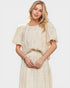 Woman wearing a beige dress with ruffled sleeves against a white background