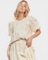 Woman wearing a cream-colored blouse and skirt set on a white background