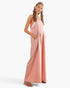 A woman modeling a dusty pink sleeveless maxi jumpsuit with wide legs and side pockets, paired with brown leather sandals, against a plain white studio background.