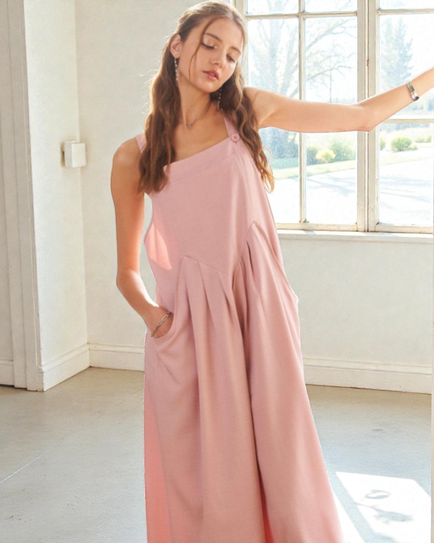 Woman wearing a pink one-shoulder dress in a bright room with large windows.