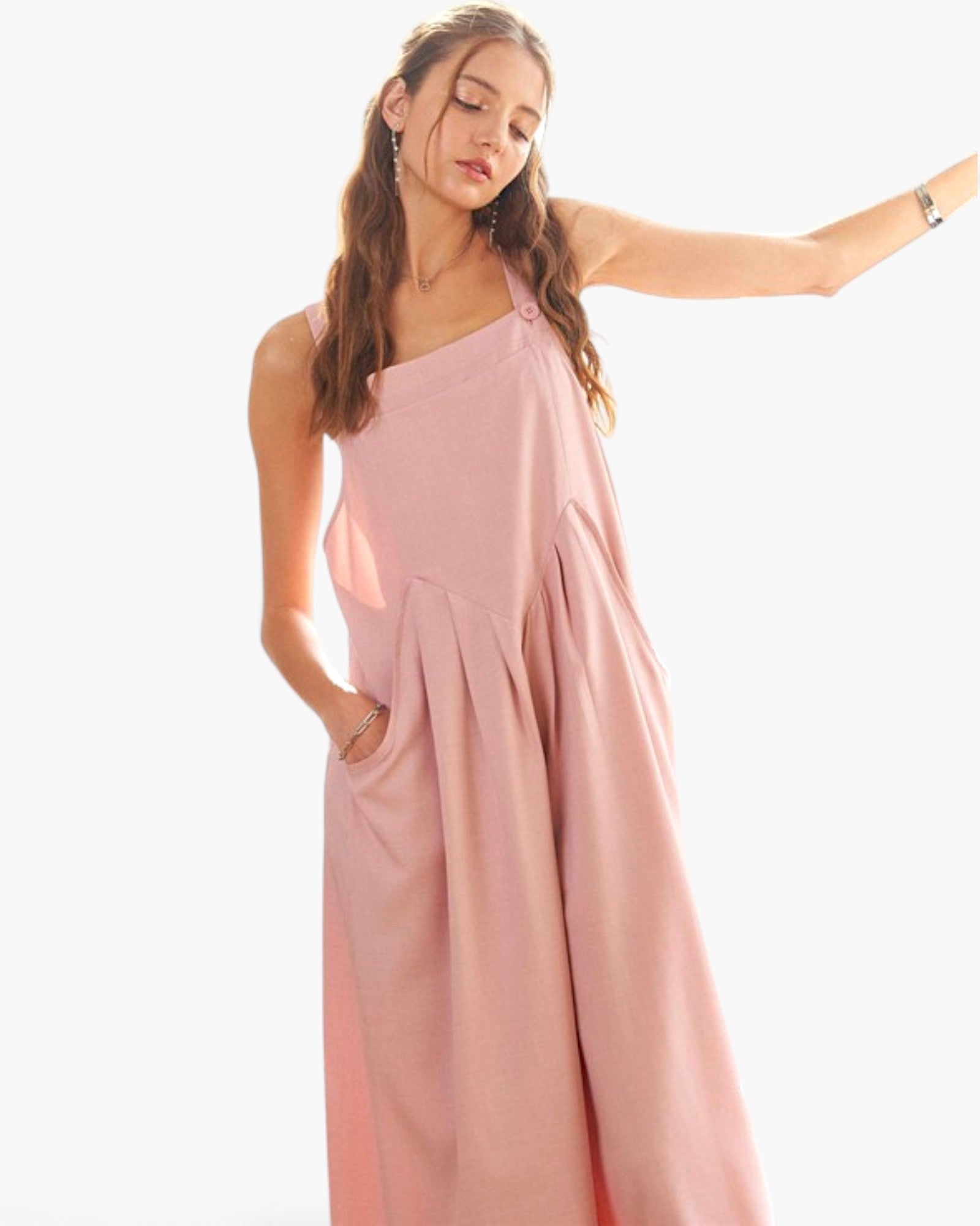 A woman modeling a dusty pink sleeveless maxi dress with a draped, wide-leg silhouette and side pockets, set against a plain white background.