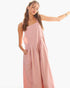 A woman modeling a dusty pink sleeveless maxi dress with a draped, wide-leg silhouette and side pockets, set against a plain white background.
